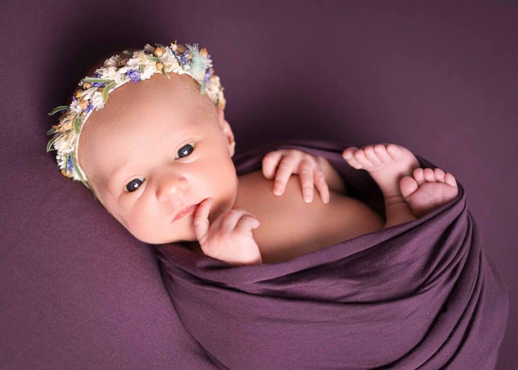 Neugeborenes Baby mit Blumenkranz im lila Tuch beim Newborn Shooting in Wiesbaden